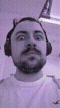 a selfie of a white person, wearing either headphones or a helmet, making an odd expression. the photo is edited to be colorized into a monochrome purple-ish color palette.