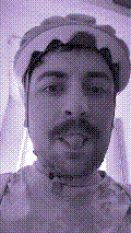 a selfie of a white person, wearing either headphones or a helmet, making an odd expression. the photo is edited to be colorized into a monochrome purple-ish color palette.