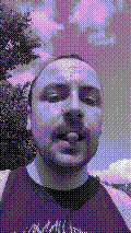a selfie of a white person, wearing either headphones or a helmet, making an odd expression. the photo is edited to be colorized into a monochrome purple-ish color palette.