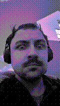 a selfie of a white person, wearing either headphones or a helmet, making an odd expression. the photo is edited to be colorized into a monochrome purple-ish color palette.