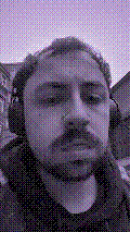 a selfie of a white person, wearing either headphones or a helmet, making an odd expression. the photo is edited to be colorized into a monochrome purple-ish color palette.