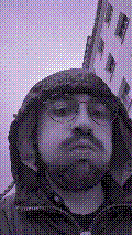 a selfie of a white person, wearing either headphones or a helmet, making an odd expression. the photo is edited to be colorized into a monochrome purple-ish color palette.