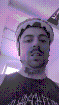 a selfie of a white person, wearing either headphones or a helmet, making an odd expression. the photo is edited to be colorized into a monochrome purple-ish color palette.